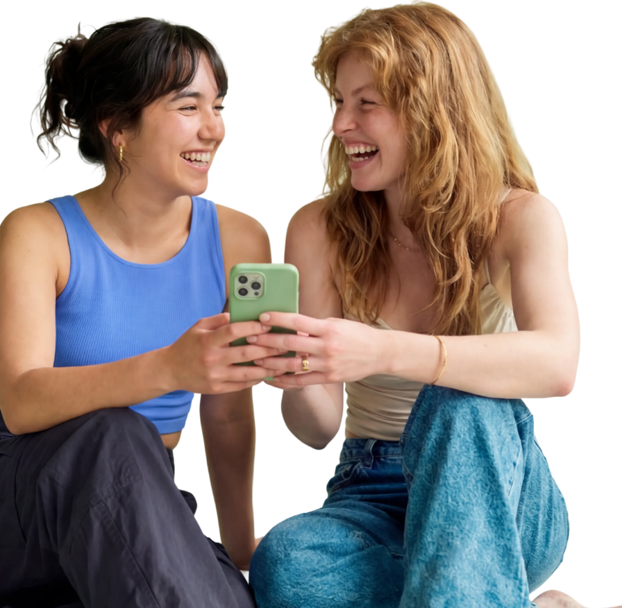 Zwei junge Frauen lachen gemeinsam, während sie zusammen auf ein Smartphone schauen