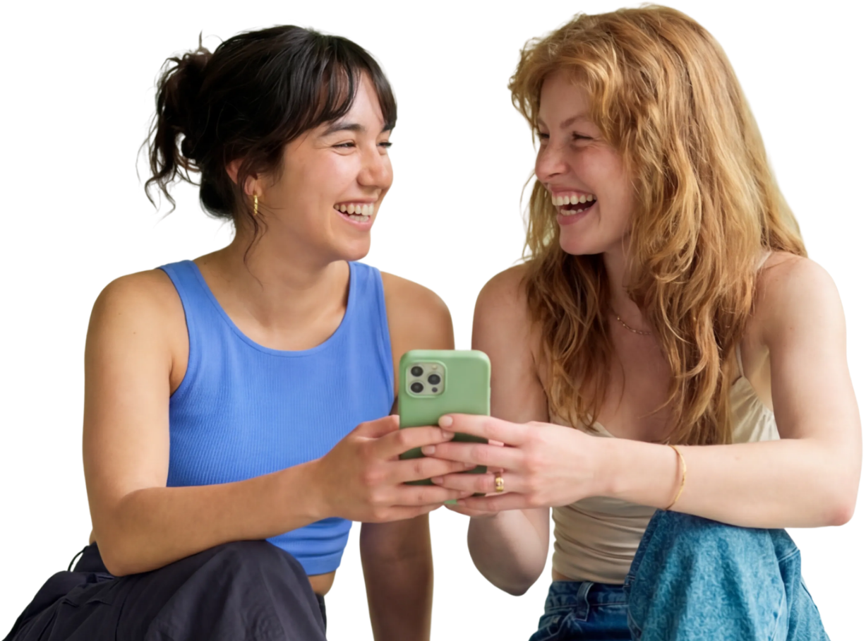 Zwei junge Frauen sitzen lachend zusammen und schauen auf ein Smartphone